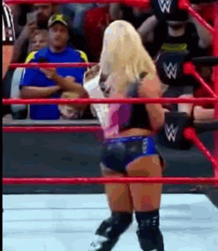 a woman is standing in a wrestling ring with a referee behind her