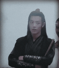 a man with long hair is standing with his arms crossed and a sword in his hand .