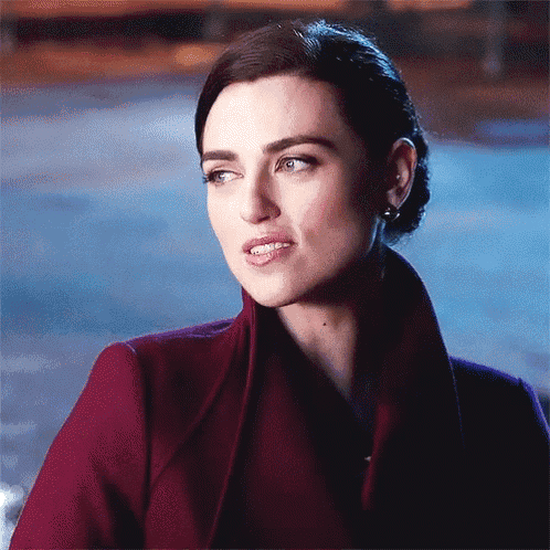 a woman wearing a red coat and earrings is looking at the camera .
