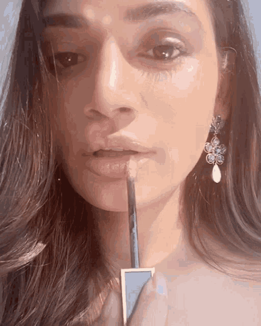 a woman wearing earrings is applying lip gloss