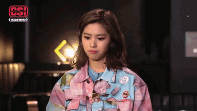 a woman wearing a pink and blue jacket with flowers on it is making a funny face .