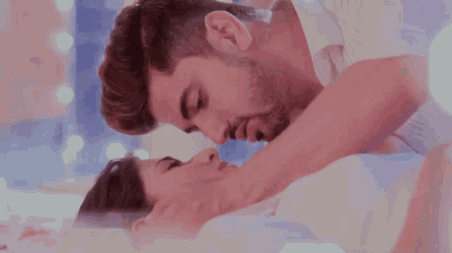 a man and woman are kissing on a bed and the man is touching the woman 's face