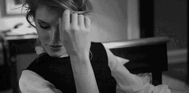 a black and white photo of a woman sitting on a couch with her hand on her head .