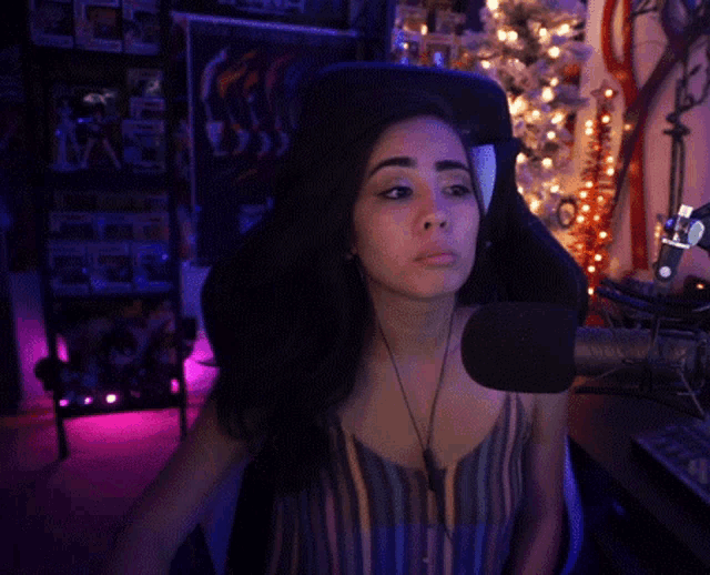 a woman sitting in a chair with a microphone in front of her and a christmas tree behind her