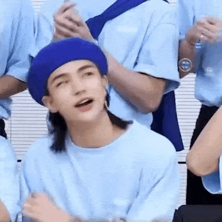 a young man wearing a blue beret and a blue shirt is sitting in a room with other people .