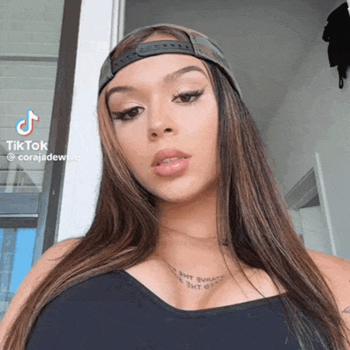 a woman wearing a baseball cap and a black tank top has a tattoo on her neck