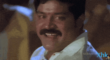 a man with a mustache is smiling in front of a xhk logo