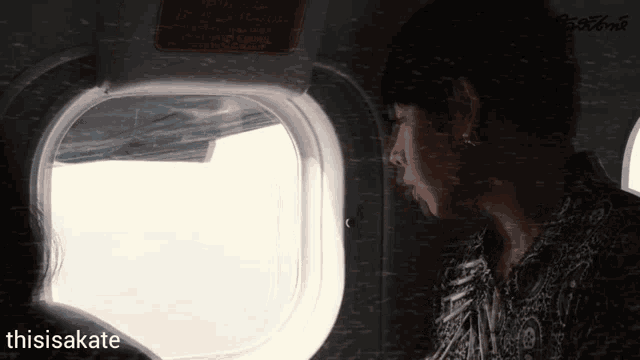 a man looking out of an airplane window with the hashtag thisisakate below him