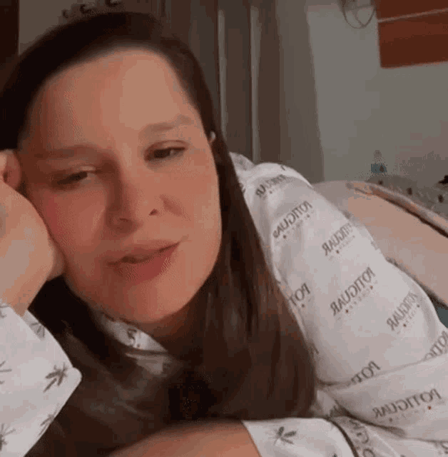 a woman in a hospital gown is laying on a bed with her hand on her chin .
