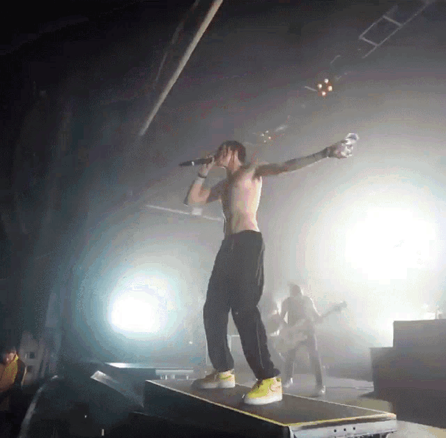 a shirtless man singing into a microphone while standing on a stage
