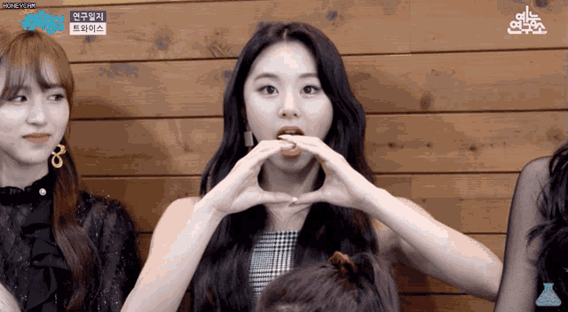 a woman making a heart shape with her hands in front of a wooden wall with a label that says honeycam