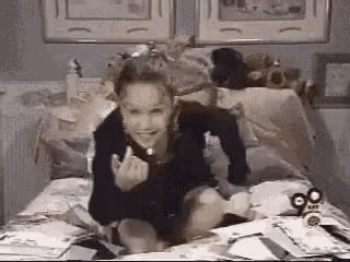 a woman is sitting on a bed with a bunch of papers on it and giving the middle finger .