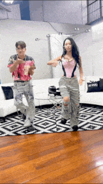 a man and a woman are dancing in front of a couch with a karl pillow on it