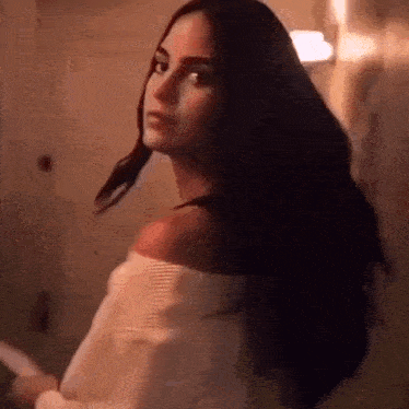 a woman in a white off the shoulder top is standing in a dark room .