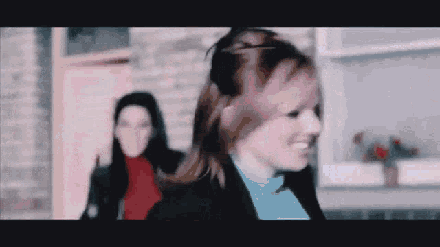 a woman in a blue sweater is smiling in front of another woman in a red sweater