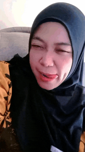 a woman wearing a black hijab making a funny face with her tongue out