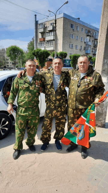 three men in military uniforms pose for a photo in front of a building