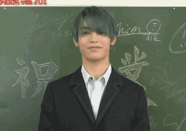 a man in a suit stands in front of a blackboard with chinese writing