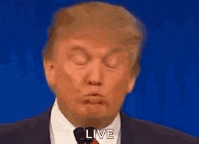 donald trump is making a funny face while talking into a microphone while wearing a suit and tie .