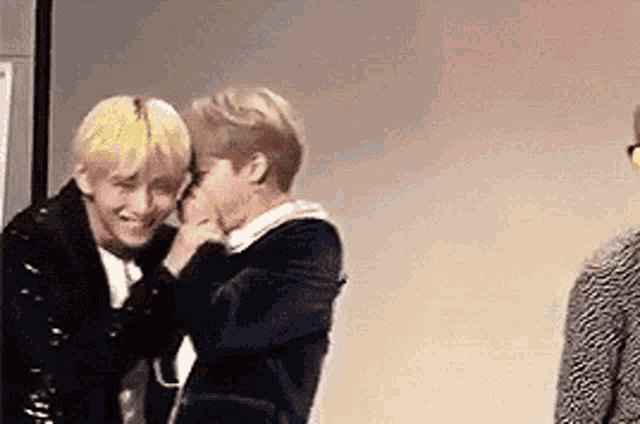 two men are hugging each other in a room while a man looks on .