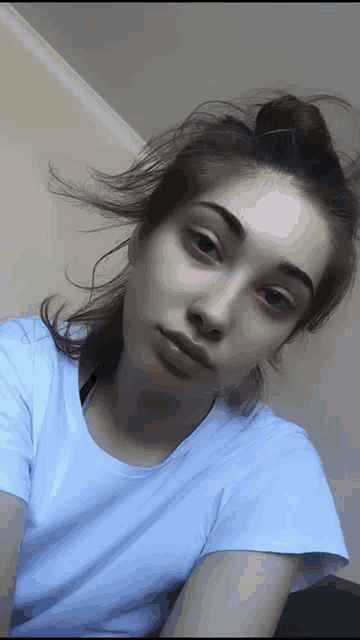 a woman in a white shirt is taking a selfie with her hair blowing in the wind