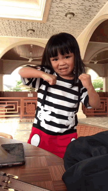 a little girl is wearing a black and white striped shirt with a mickey mouse on it