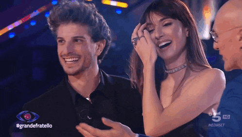 a man and a woman are laughing in front of a sign that says grande fratello