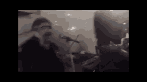 a man is singing into a microphone in a dark room while another man plays a keyboard .