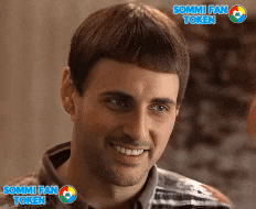 a man is smiling in front of a sommi fan token sign