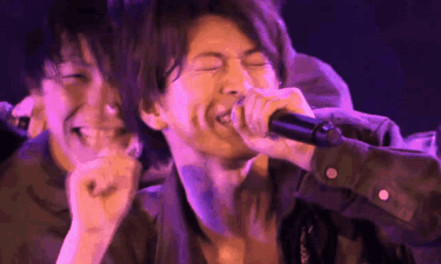 a man is singing into a microphone on a stage while another man laughs behind him .