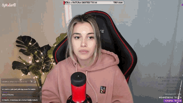 a woman in a pink hoodie is sitting in front of a red microphone and a sign that says trt 1500