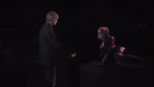 a man and a woman are standing next to each other in a dark room holding hands .