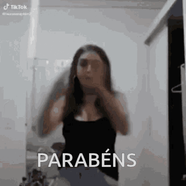a woman is standing in front of a mirror in a bathroom with the words parabéns written on her face .