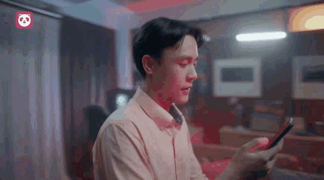 a man in a pink shirt is looking at a cell phone
