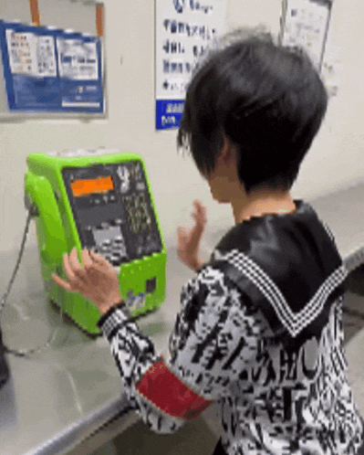 a person talking on a green pay phone with a sign on the wall behind them