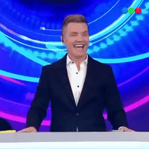 a man in a suit is laughing while standing in front of a blue background