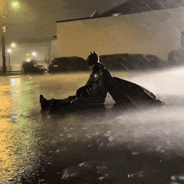 a man in a batman costume is laying in the rain