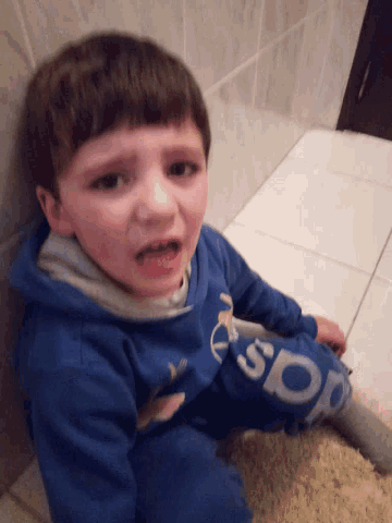 a young boy wearing a blue adidas sweatshirt lays on the floor