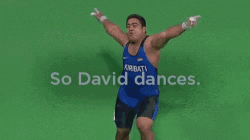 a wrestler is jumping in the air with the words so david dances behind him .