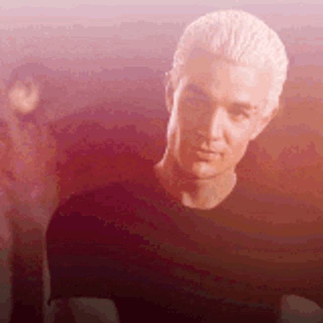 a man with blonde hair is wearing a black shirt and looking at the camera