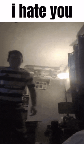 a man in a striped shirt is standing in a dark room with the words i hate you above him