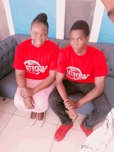 a man and a woman are sitting on a couch wearing red shirts with the word believe on them