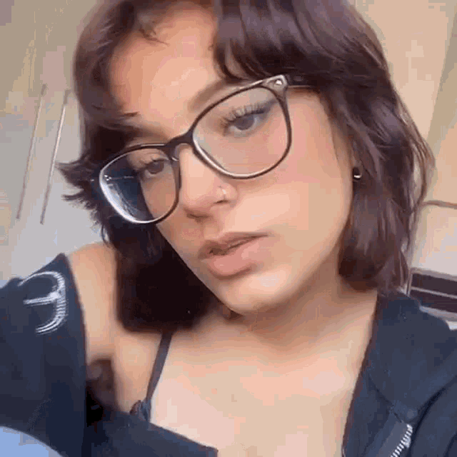 a girl wearing glasses and a nose ring is taking a selfie .
