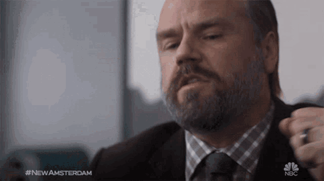 a man with a beard is being adjusted by another man in a suit and tie with the hashtag #newamsterdam