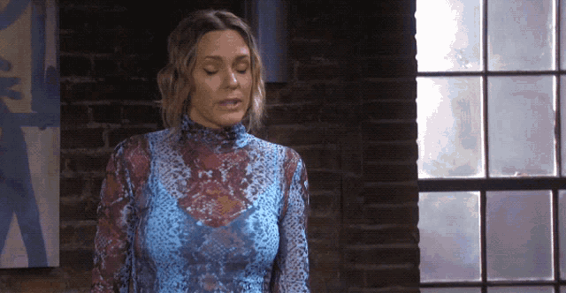 a woman in a blue and red snake print top stands in front of a window