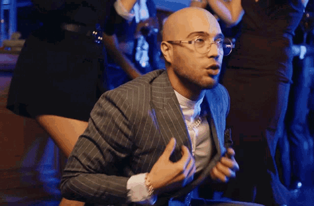 a bald man wearing glasses and a suit is dancing at a party