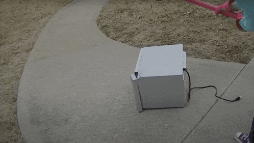 a person is using a pink hammer to smash a microwave on the sidewalk