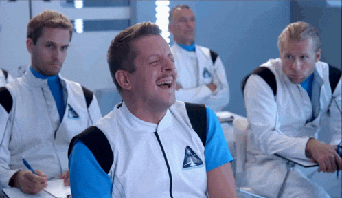 a man in a space suit is laughing in a classroom with other men