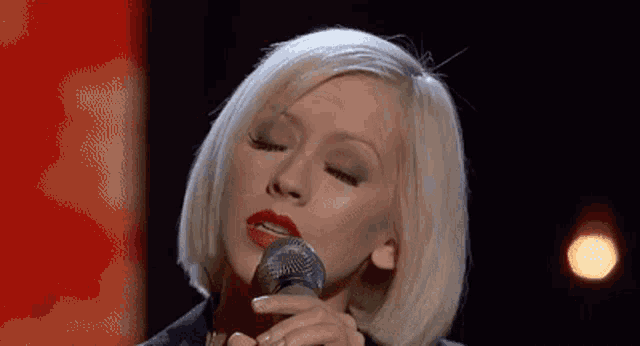 a woman is singing into a microphone with her eyes closed
