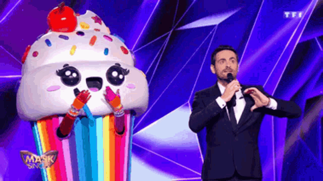 a man in a tuxedo stands in front of a cupcake mask on a stage